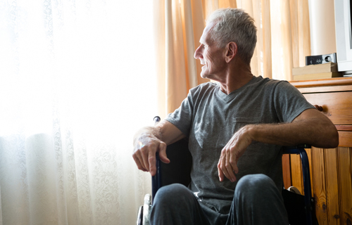 Senior man in a wheelchair looking out a window.