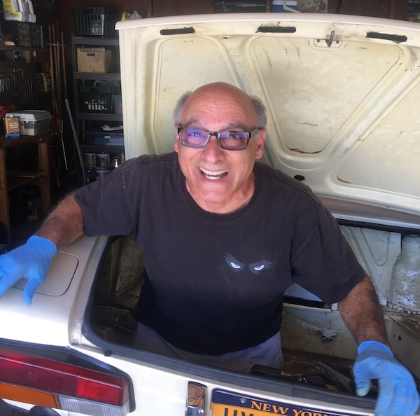 Larry stands on the ground through the trunk of his nephew’s Fiat after they had removed the fuel tank.